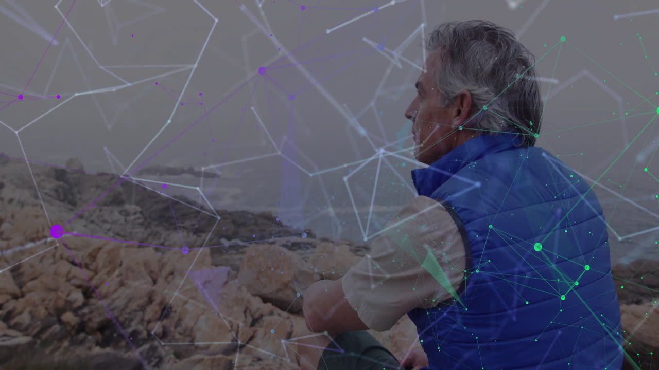 Senior man sitting on rocky shoreline gazing toward ocean, featuring glowing tech network overlay