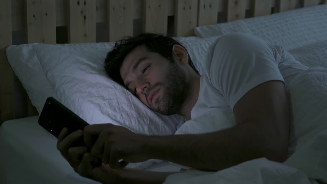 joven deprimido y somnoliento de oriente medio. personas que usan un teléfono inteligente en las redes sociales internet y duermen en la cama en el dormitorio en casa. estilo de vida a última hora de la noche en el concepto de dispositivo tecnológico.