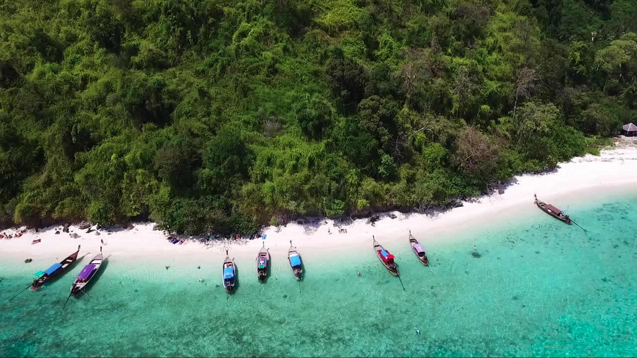 열대 섬의 모래사장에 늘어선 전통 태국 보트의 드론 샷