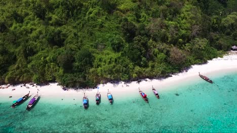 Drohnenaufnahme-Traditioneller-Thailändischer-Boote,-Die-An-Einem-Sandigen-Ufer-Einer-Tropischen-Insel-Aufgereiht-Sind