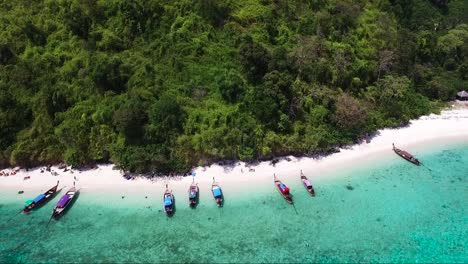 drone shot of traditional thai boats lined up on a sandy shore of a tropical island