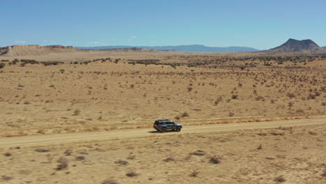 aerial following suv down dirt road with wide open desert landscape behind