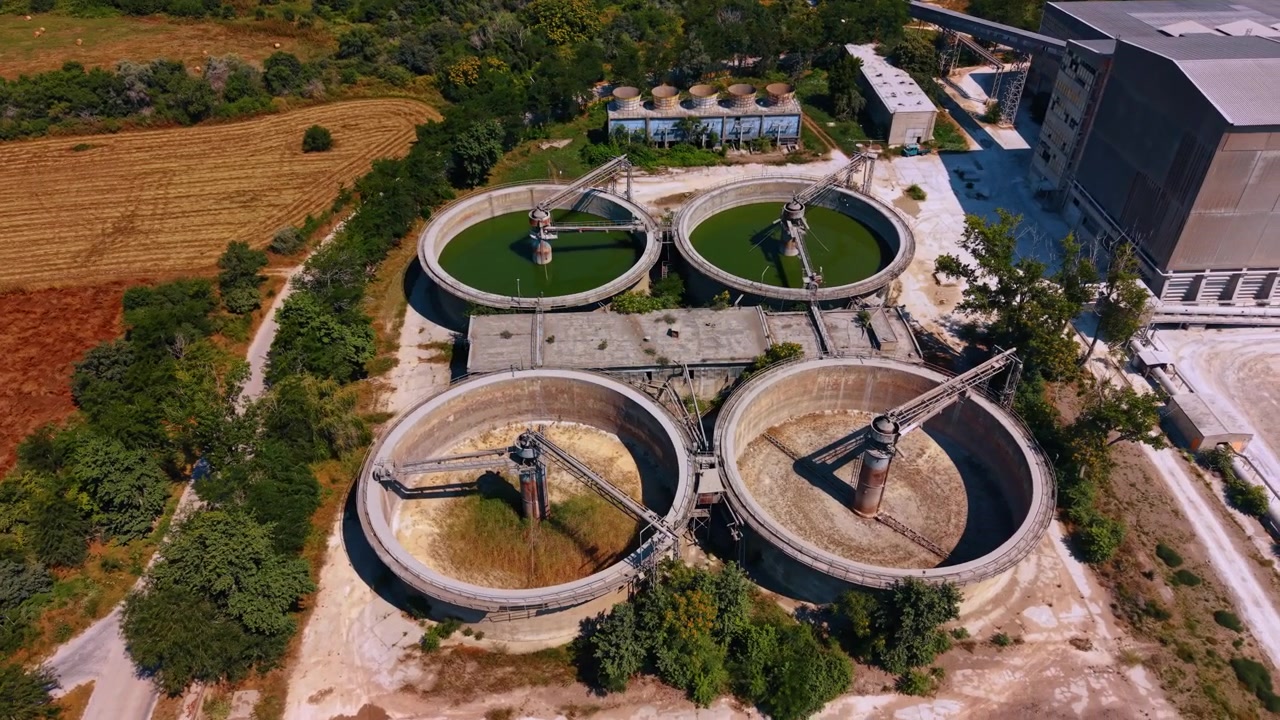 Industrial water treatment facility near rural fields with large tanks. The facility shows three large water treatment tanks surrounded by fields and buildings in the background.