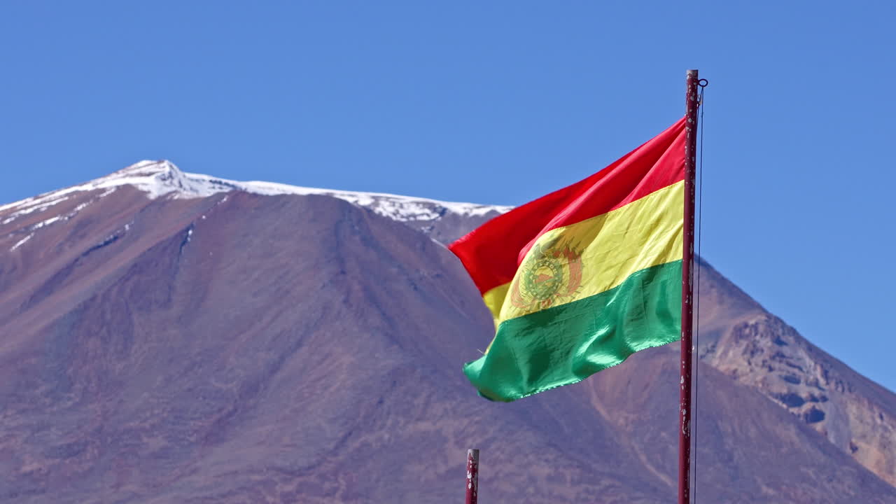 la bandera de bolivia ondea en el viento balanceándose con el pico de la montaña cubierto de nieve detrás
