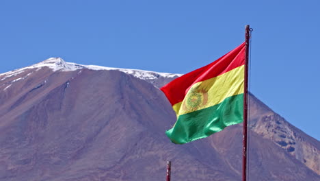 la bandera de bolivia ondea en el viento balanceándose con el pico de la montaña cubierto de nieve detrás