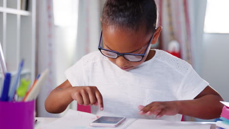 Una-Joven-Con-Gafas-Sentada-En-Un-Escritorio-En-El-Dormitorio-Jugando-En-El-Teléfono-Móvil