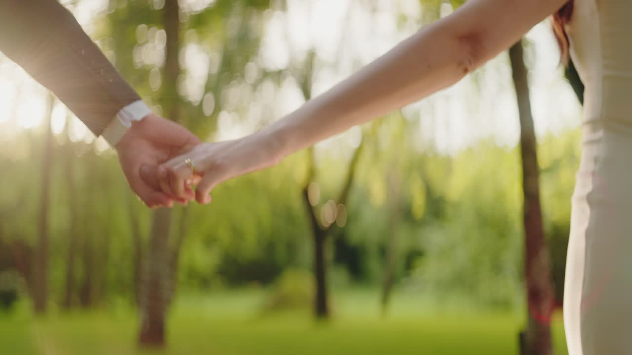 Bride and groom’s hands clasped together in intimate outdoor moment under soft natural light
