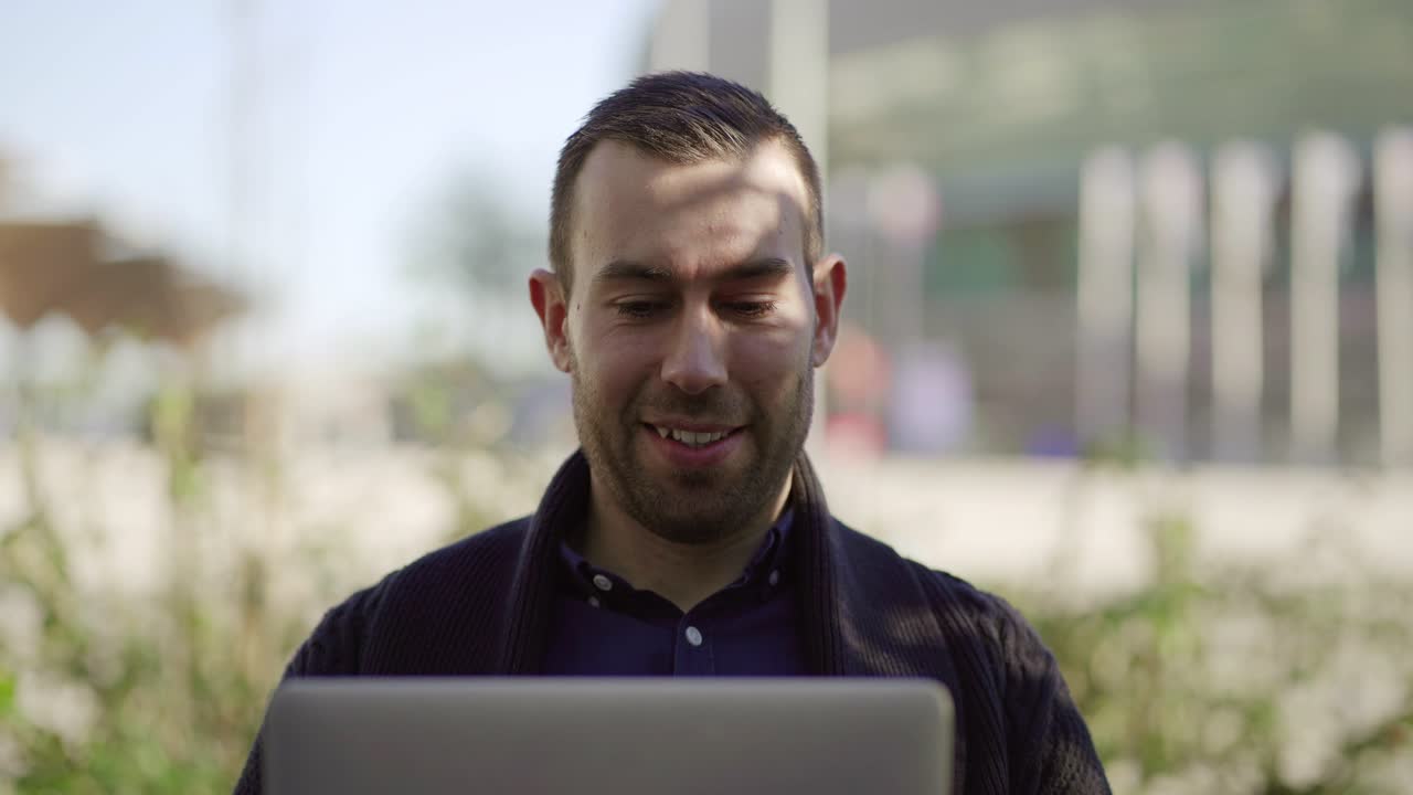 hombre guapo exitoso sentado en el parque con una computadora portátil