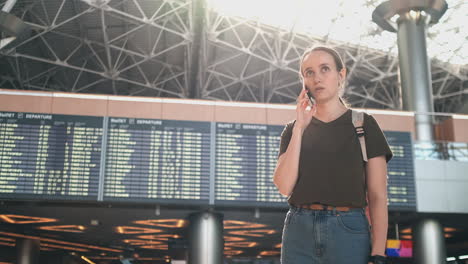 a woman traveler with a backpack at the airport discusses the delay of his flight on the phone. transfer and delay of departure from the airport