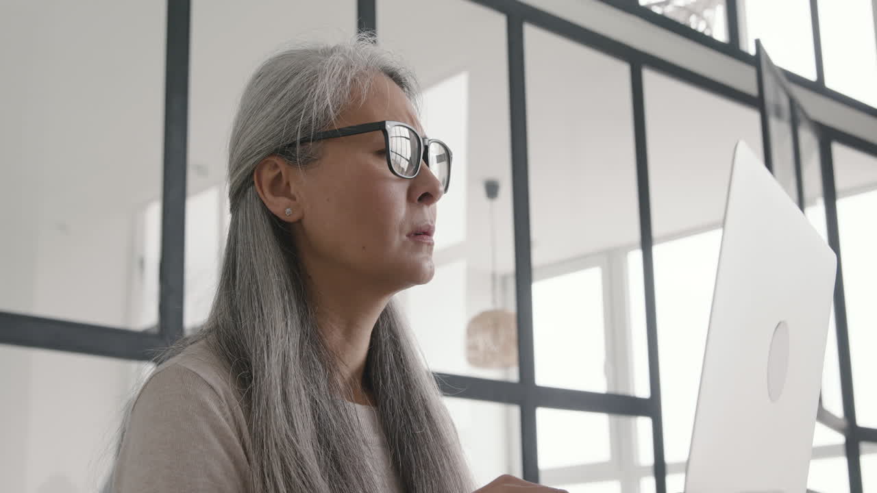 mujer de mediana edad con dolor de cabeza mientras trabaja en una laptop sentada en un sofá en casa 1