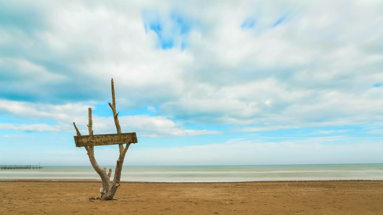 Time lapse of the clouds on the sandy beach. You can see the board of the bar called Gradela. It's partly sunny and partly cloudy. Taken by the sea of   Italy, Rimini. Beautiful natural landscape