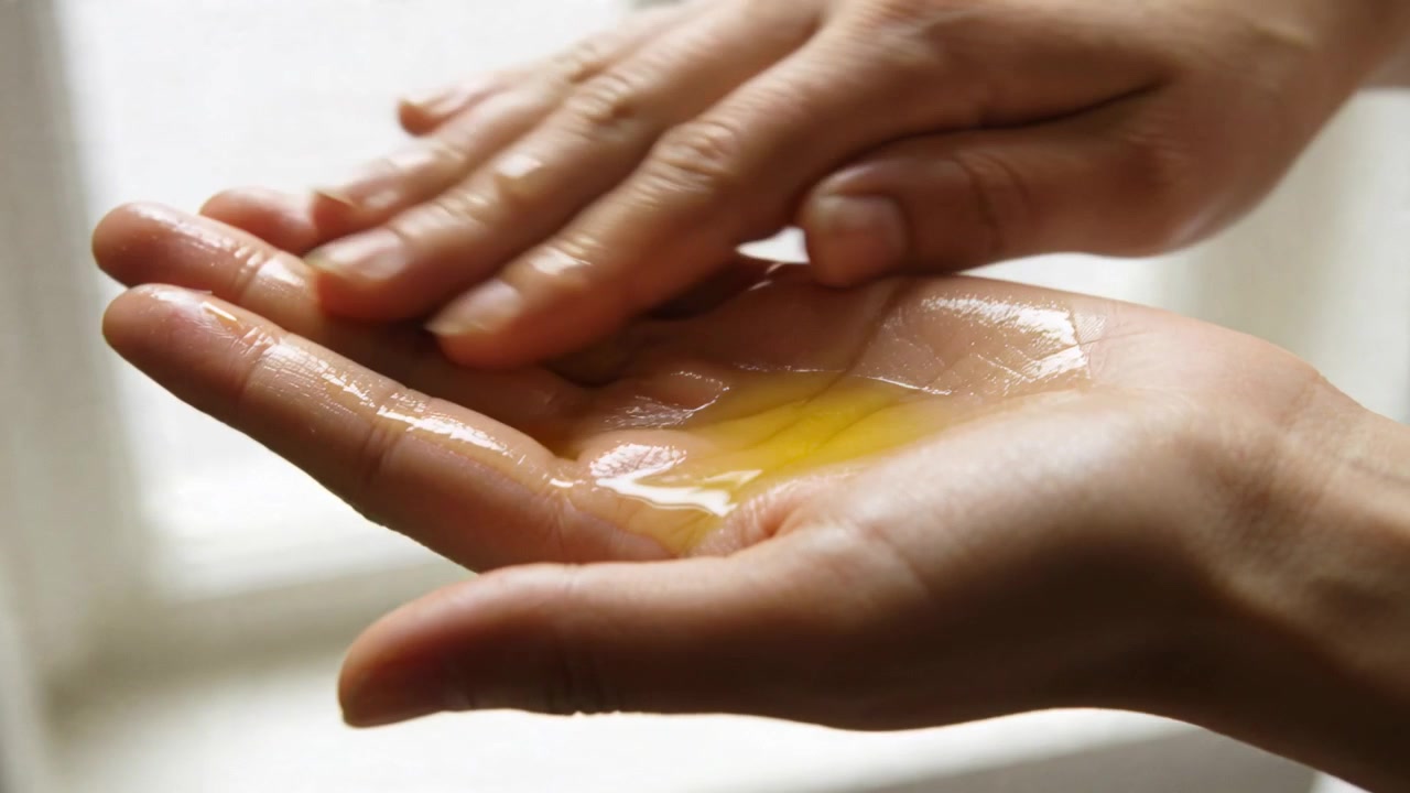 Dedos tocando manos adultas, frotando líquido transparente sobre la palma ahuecada junto a la ventana para mezclar la yema.