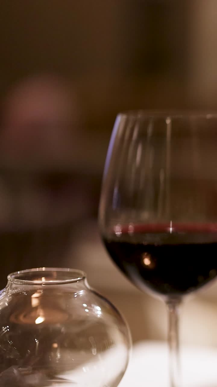 A man uses his phone at a restaurant table with wine, creating a relaxed, intimate atmosphere with soft lighting