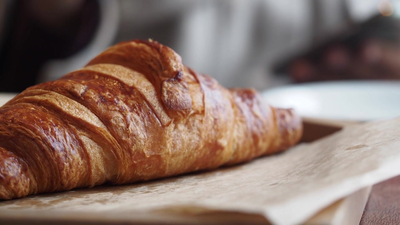 Primo piano di un cornetto dorato con caffè sullo sfondo