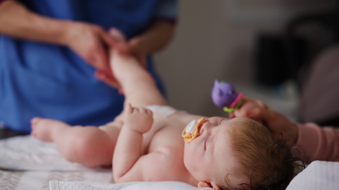 Yetişkinlerin nazik kol ve bacak hareketlerine yardımcı olduğu, sırtüstü yatan, emzikli bebek