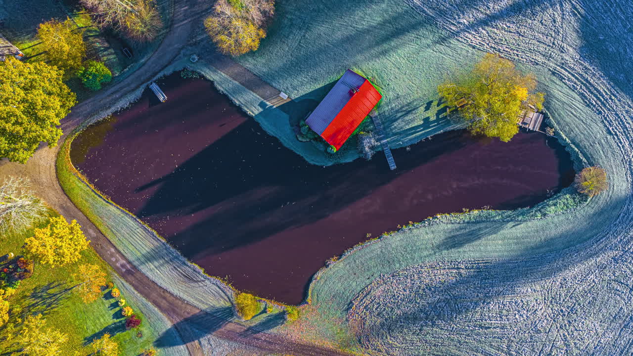 Aerial view of red-roof house by a pond, autumnal setting, unique mood