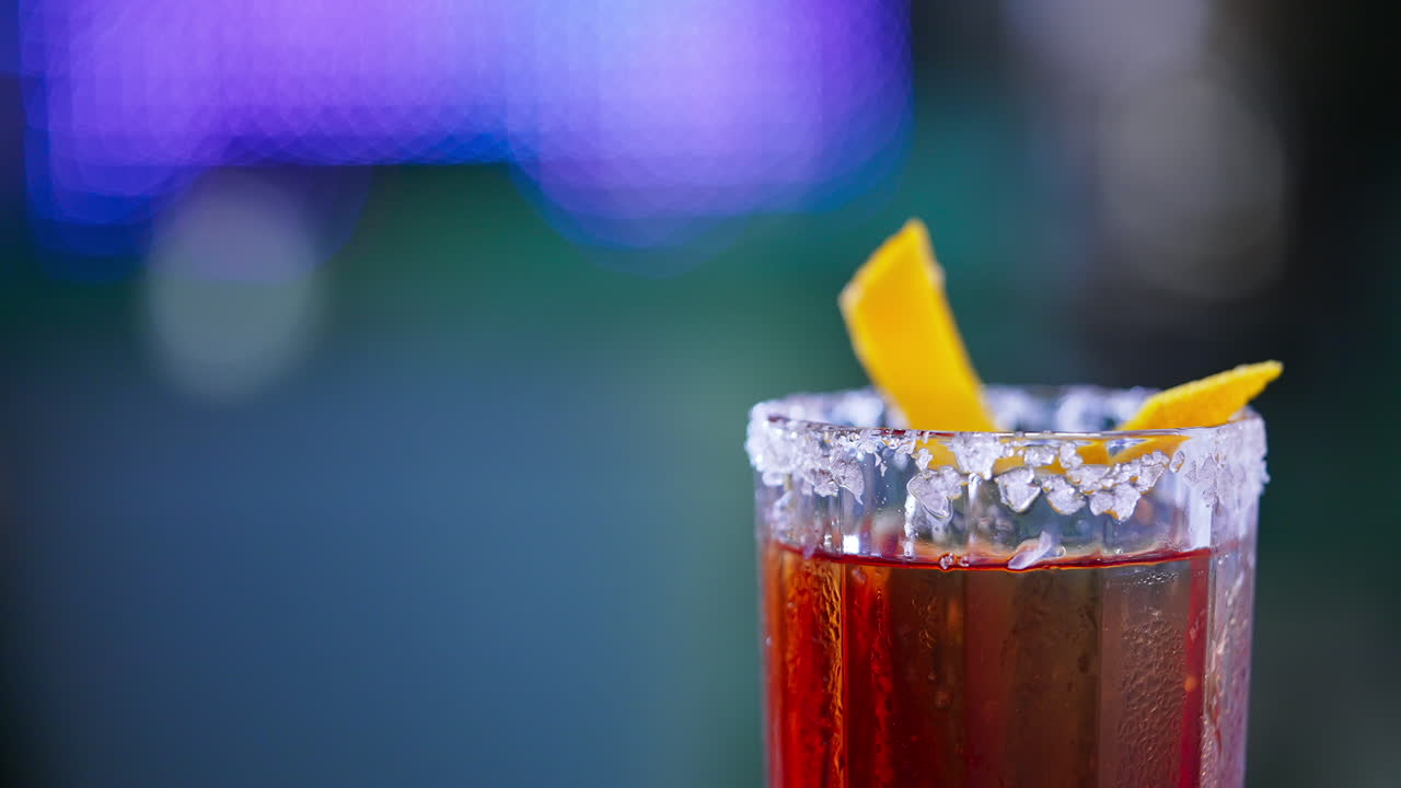 Rotating glass with top decorated with salt and orange peel. Red alcohol cocktail in the bar. Close up. Blurred backdrop.