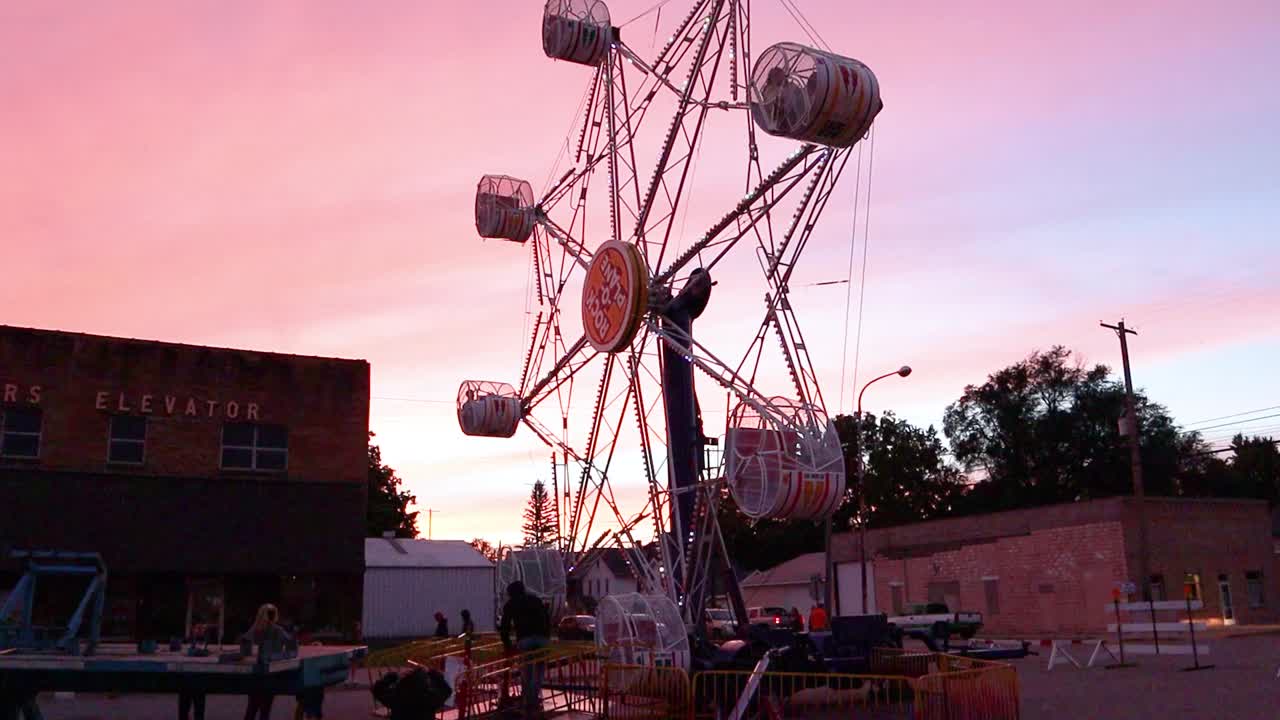 A carnival ferris wheel turns to allow people to exit the ride at dusk.