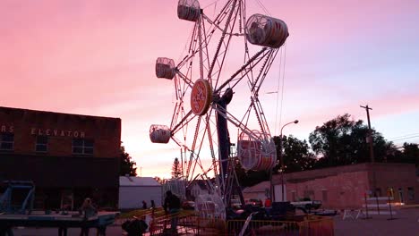 a carnival ferris wheel turns to allow people to exit the ride at dusk.