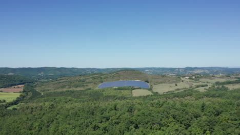 Aerial-truck-shot-of-the-green-countryside-with-a-small-solar-farm-on-the-horizon,-bright-sunny-daylight