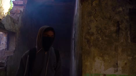 vista frontal en cámara lenta de un hombre cubierto de pies a cabeza, usando una bolsa y una máscara, sosteniendo un iluminador de fuego para encontrar su camino a través del camino oscuro y espeluznante de un interior de un lugar antiguo