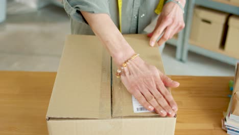 vista de primer plano de las manos femeninas envolviendo un paquete, cerrando una caja y poniendo la factura mientras prepara el pedido para el envío en la tienda en línea