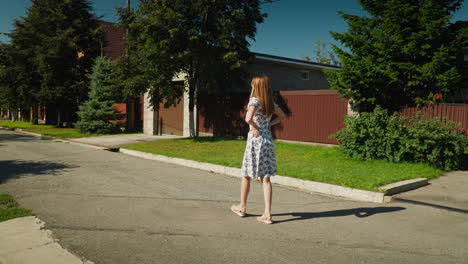 side view of woman walking confidently with hands on waist in peaceful suburban neighborhood, wearing floral dress under clear sky, expressing elegance and pride through posture and motion