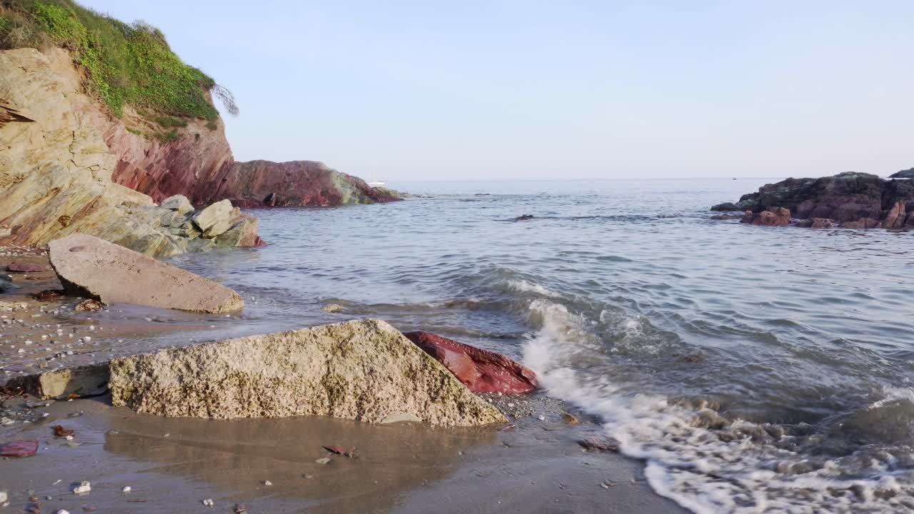 Gentle beach waves around rocks on a sunny day Talland Bay, Cornwall