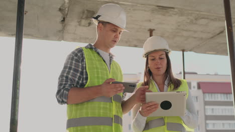 Edificio-En-Construcción-Con-Una-Mujer-Y-Un-Hombre-Constructores-Ingenieros-Constructores-Caminando-A-Lo-Largo-De-él.-Edificio-En-Construcción-Con-Una-Mujer-Y-Un-Hombre-Ingenieros