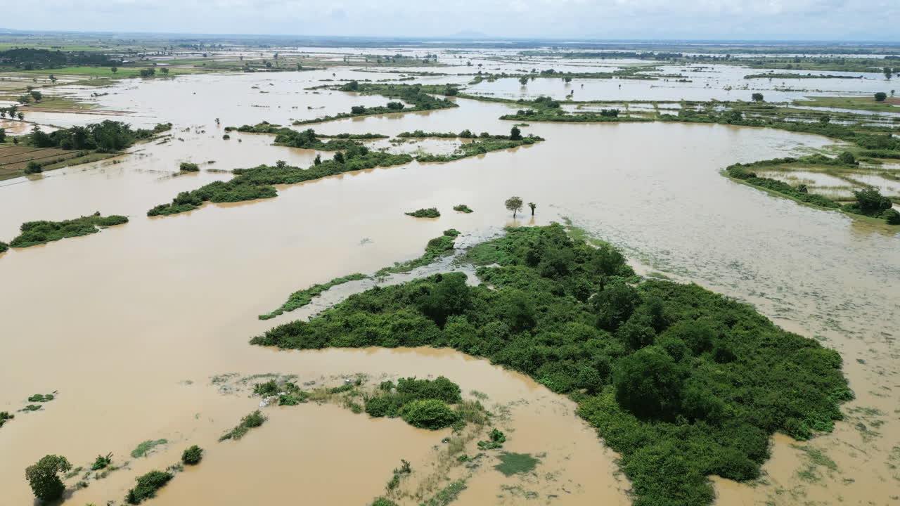 Aerial shot of muddy floodwaters surrounding small green islands in rural Cambodia
