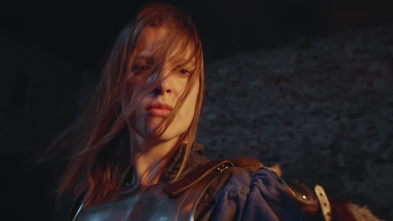 una mujer medieval con cabello largo y suelto bajo el resplandor de una antorcha parpadeante