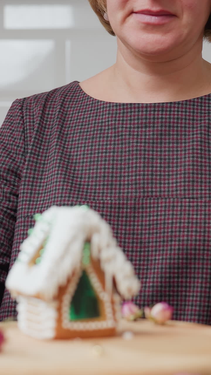 mujer en vestido a cuadros sentada en la cocina, girando cuidadosamente el pastel decorado en una bandeja de madera, luz de vela cálida, backsplash de azulejos blancos, hervidor eléctrico y cocina rústica