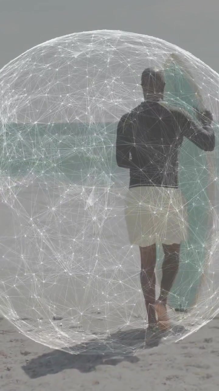 Vertikální video: Muž kráčí po břehu drží prkno, AR koule ho obklopuje, připravuje se na surfování s pomocí technologie.