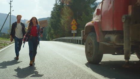 Tourists-trekking-hiking-car-on-countryside-road.-Hitchhikers-hold-sign-outside.