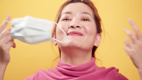 cierra a una mujer asiática sonriendo y quitándose la máscara protectora para tomar aire fresco después de que la situación de civid-19 se deshaga con el fondo amarillo