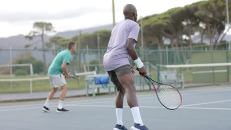 two diverse male friends playing doubles returning ball on outdoor tennis court in slow motion