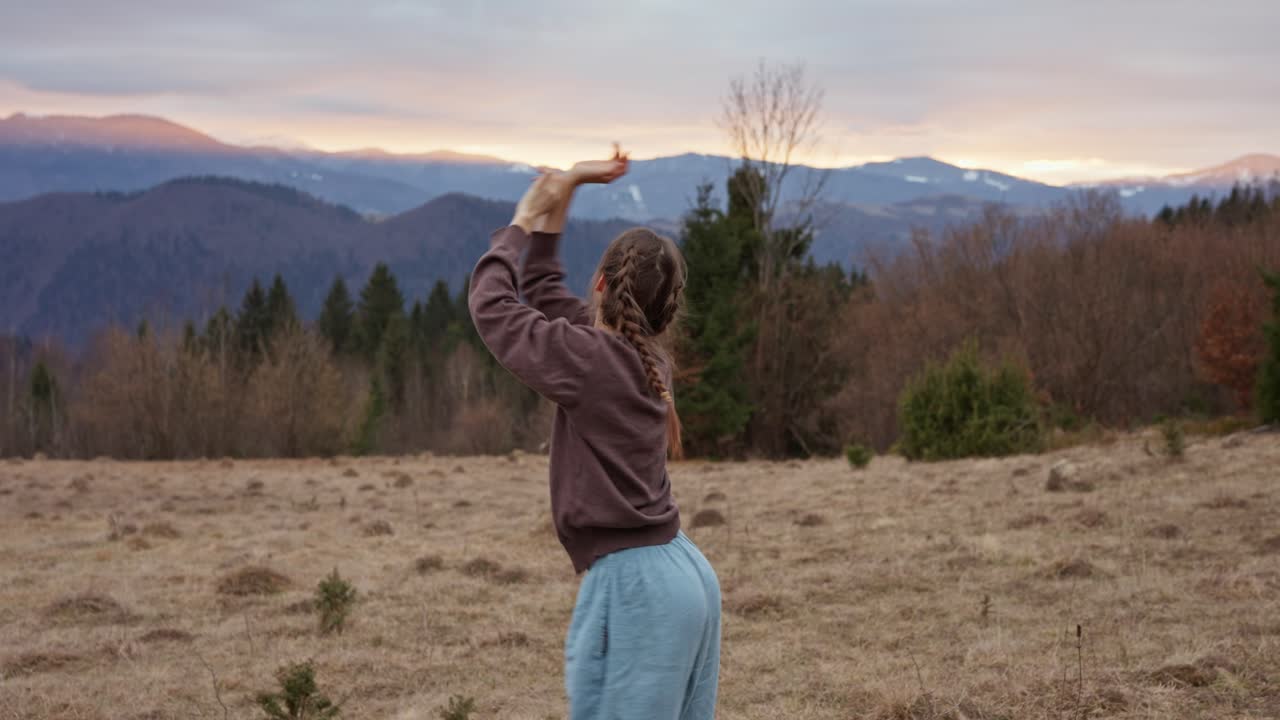 A woman stretching in a field with mountains in the background