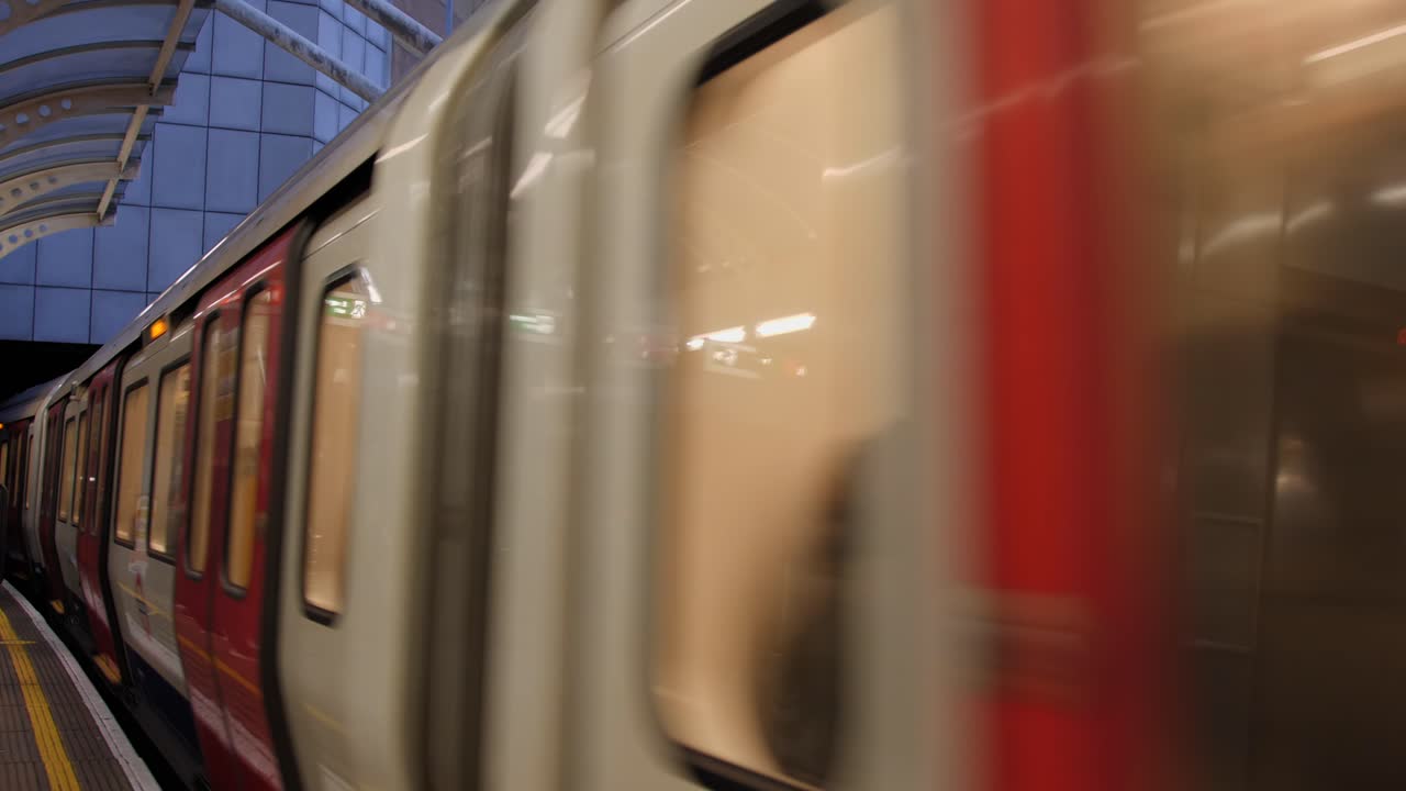 Red London Underground train arriving at Hammersmith station with bright platform advertising