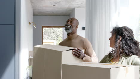 happy biracial couple talking and carrying cartons at new house, slow motion