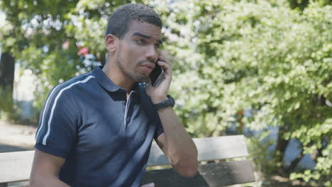 Agitated-man-sitting-on-bench-outside,-talking-on-phone,-arguing