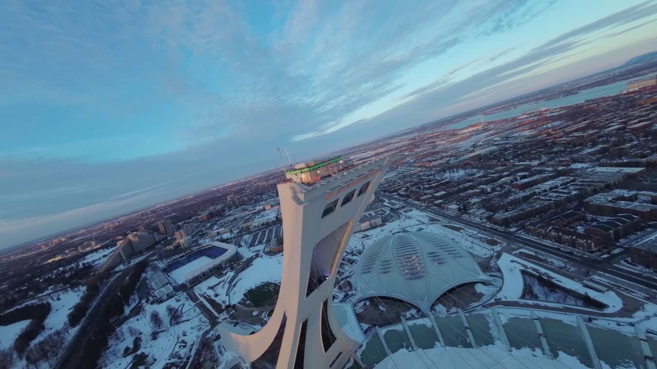 FPV drone swooping over Montreal Olympic Stadium at sunset with snow on roof, capturing winter views