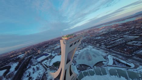 fpv drone swooping over montreal olympic stadium at sunset with snow on roof, capturing winter views