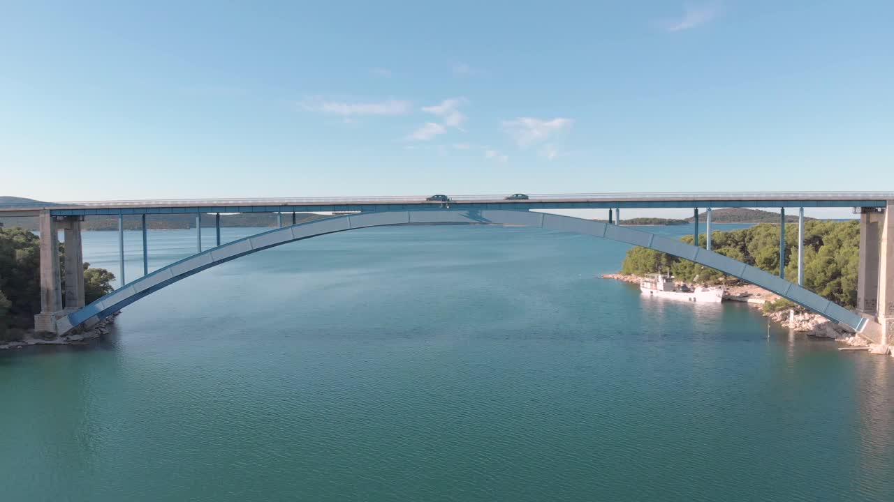 Aerial drone view of two car chase on a highway bridge over the sea ocean clear blue sky and mountain landscape.