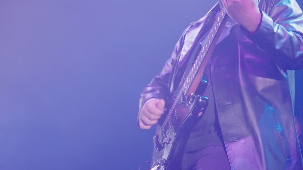 Primo piano di un musicista che suona la chitarra elettrica sul palco con luci viola.