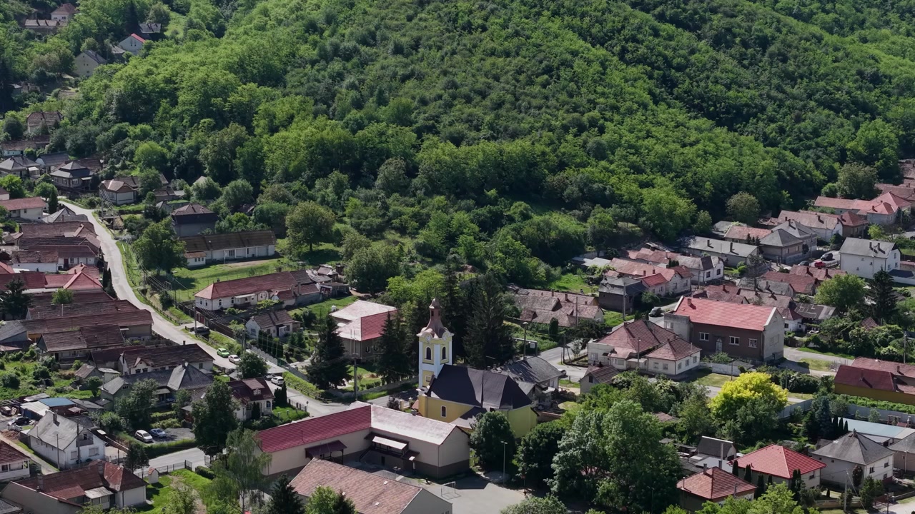 Letecký pohled zachycuje malou maďarskou vesnici obklopenou bujnými zelenými lesy a zvlněnými kopci.