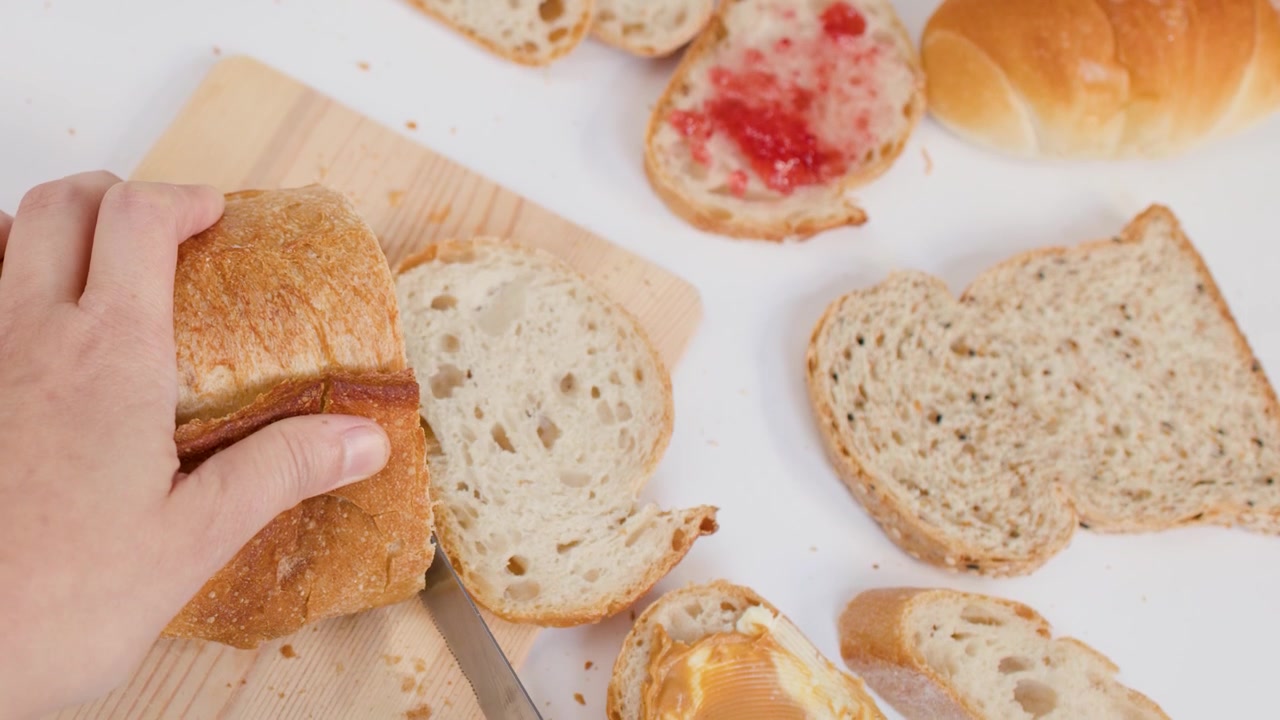 Primo piano di mani che usano un coltello per affettare pane croccante su un tagliere di legno