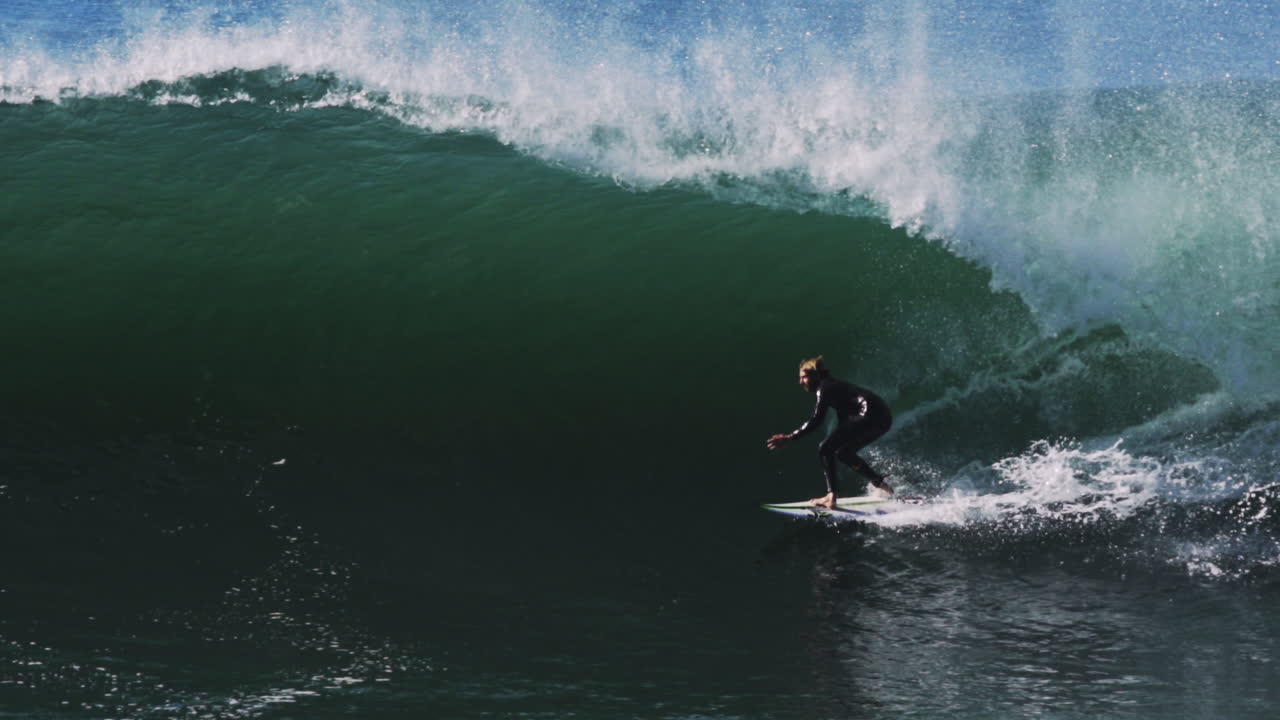 High-speed telephoto of surfer gliding through thick wave barrel before whitewater hits
