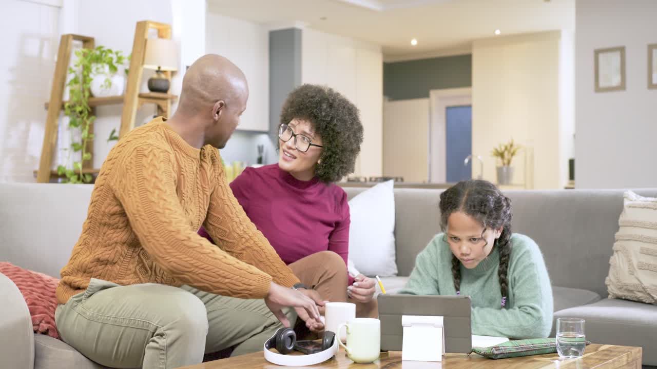 African American family starting homework with child writing on tablet, parents helping on couch