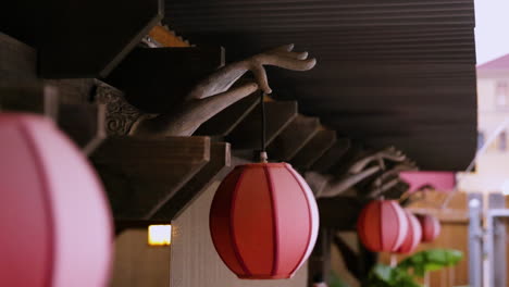 closeup of red lanterns hanging from a wooden structure with hand sculptures