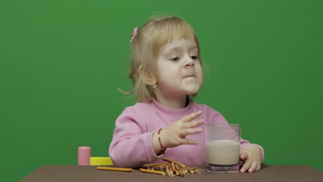 the child eats cookies. a little girl is eating cookies sitting on the table.